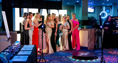 Large group of women in formal wear posing for a photo in front of giant letters spelling out heart.